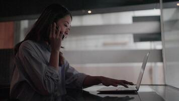 Determined businesswoman working late at night with laptop and mobile phone in modern office. The dimly lit atmosphere creates a quiet atmosphere of concentration and dedication. video
