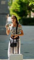 A cheerful traveler enjoys a refreshing drink while carrying their luggage in an urban setting video