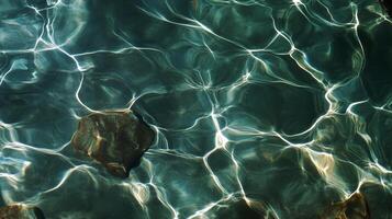 Clear water ripples reflect sunlight, revealing a stone beneath the surface in a tranquil setting photo