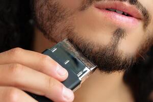 Man trimming his beard indoors using an electric trimmer while showcasing his personal grooming routine photo