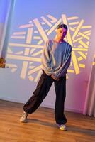 A young person stands in a studio with a patterned projection on the wall behind them photo