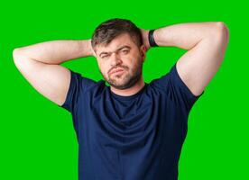 A man poses confidently with his hands behind his head against a bright green background photo