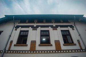 Historic building facade with three windows, intricate brickwork, and decorative elements under a cloudy sky photo