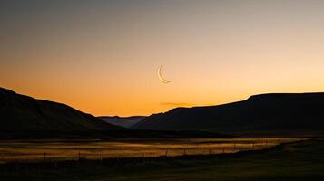 Stunning crescent moon sets against a tranquil landscape at dusk near mountainous terrain photo