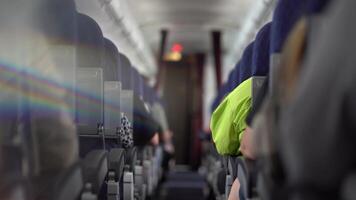 People are sitting with their backs to the camera in the cabin of a passenger plane right down the aisle. Daylight in the cabin. Through a glass prism rainbow video
