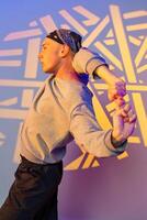 A young man in a bandana dances against a wall with geometric patterns projected on it photo