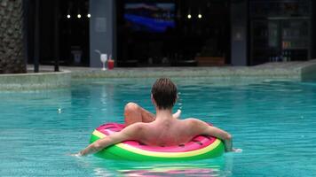 Back view of man floats in the pool with an inflatable ring, enjoying a moment of relaxation. This scene embodies the spa concept, perfect for themes of leisure and wellness. video