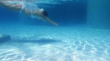 Side view of fit female dives in the pool. Underwater view of the girl diving in the pool and gliding underwater with bubbles. Summer holiday concept. Luxury pool on vacation at tropical resort spa. video