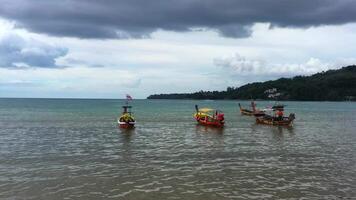 Boats in the ocean near the coast of Phuket island. Tropical empty beach. Small wooden fishing boats anchored close to the shore. Unspoiled exotic beach. Calm turquoise ocean waters. Drone aerial view video