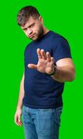 A man with a serious expression holds up both hands in a stopping gesture against a bright green background photo