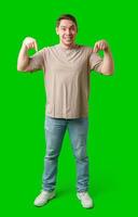 Cheerful young man pointing downwards in a casual outfit against a vibrant green backdrop photo