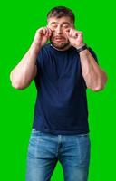 Man expressing frustration with tired eyes while standing in front of a bright green background photo
