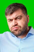 A man with a serious expression wearing a light blue shirt poses against a bright green background photo