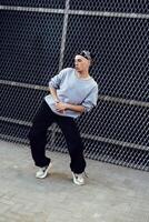 A man dances in front of a chain link fence, wearing a grey sweatshirt, black pants, and white sneakers photo