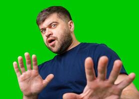 A man with a serious expression holds up both hands in a stopping gesture against a bright green background photo