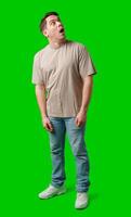 A surprised man stands in front of a bright green screen, expressing shock with his mouth open photo