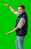 Man in a navy vest gestures enthusiastically toward a green screen photo