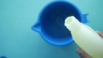 A person is transferring liquid from a bottle into a blue container in a kitchen environment video