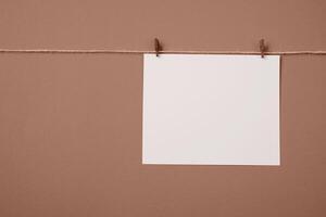 Mocha Mousse - color of the year 2025. Note paper card hanging with wooden clip or clothespin on rope string peg isolated photo