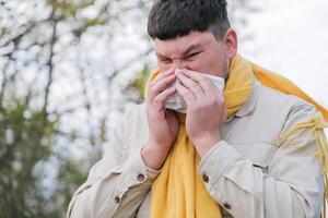 young man enjoying autumn days breathing fresh air using tissue to wipe nose photo