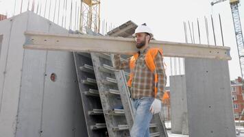 Builder man in hardhat and vest carrying timber on building site in his working day video