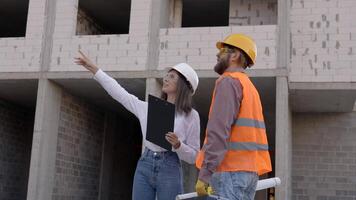 Female architect pointing at something while discussing with construction worker at building site video