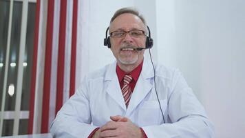 Happy doctor looking at camera. Doctor man sitting at the desk at his working place and smiling at camera video