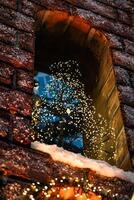 A small Christmas tree stands on the window of a brick building. New Year photo