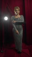Portrait, attractive model poses in front of camera in expensive silver jewelry and luxurious shiny dress during photo shoot against background of red curtain and spotlight video