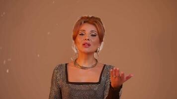 Attractive young singer performs New Year and Christmas songs against abstract white backdrop. She is illuminated by warm lights, and soft snowflakes fall around her. video