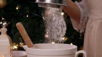 Rye white flour is poured and sifted through sieve, then it falls into ceramic mixing bowl. pastry chef is preparing Christmas treats for festive table. Slow motion video