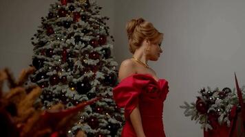 Portrait of beautiful woman, dancing gracefully and gazing directly into camera, is shown. In background, Christmas tree is decorated with garlands and ornaments. video