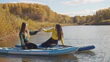 Two young women are attempting to create heart shape with their hands while riding surfboard. Current is carrying them in different directions video