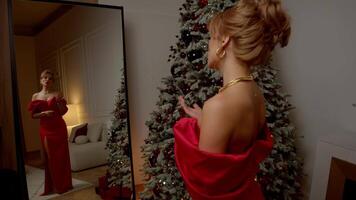 Beautiful, statuesque, and graceful woman, wearing an elegant red dress that reaches floor, stands in front of mirror, singing song, she prepares to celebrate Christmas or New Year. video