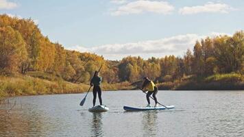 Young woman is trying stand up paddleboarding for first time. She stands up on board and tries to keep her balance, not wanting to fall into cold water. video