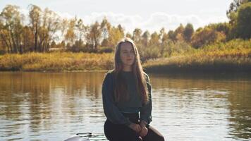 Portrait of attractive young woman enjoying her favorite outdoor activity, paddleboarding. She is sitting on board and looking directly at camera, enjoying experience video