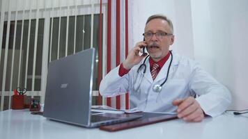 Doctor talking on mobile phone. Mature doctor talking with patient on mobile phone video