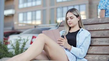 Young woman using tablet on bench in urban setting video