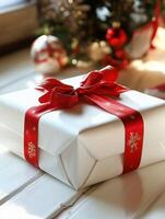 White christmas gift box wrapped with red ribbon near decorated christmas tree photo