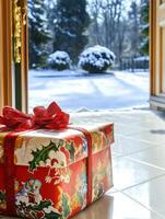 Christmas gift wrapped with red ribbon sitting by open door showing snowy garden photo