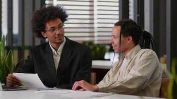 Two multiracial business men African American businessmen partners diverse colleagues males discuss financial data analyzing documents marketing project result report use laptop talk at office desk video