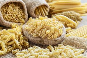Various types of pasta displayed on burlap of fusilli, spaghetti, farfalle, and semolina photo
