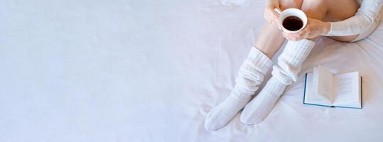 Lazy time in bed. Young woman in knitted knee socks on a white sheet reading photo