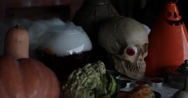 assustador decorações com crânio e dia das Bruxas jack-o-lanterna dentro escuridão. olho do crânio parece para Magia poção borbulhante e fumar. dia das Bruxas feitiçaria adereços e abóboras em mesa video