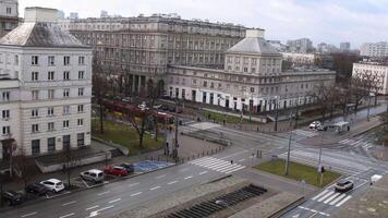 View of urban area in Warsaw with distinct architecture, parked cars, and bustling streets in winter. Tram turn at intersection. Dynamic daily life of the city Warsaw Poland 12 12 2024 video
