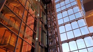 Corporate building walls in golden hour sunlight. Modern elevators move down and rise up by heavy steel supporting constructions. Mirrored walls of business skyscraper video