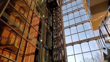 Corporate building window wall with abstract geometric reflections and golden hour sunlight. Modern glass elevator rises up and goes down in time lapse. Mirrored walls of business skyscraper video