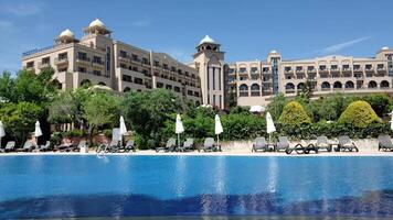 Time lapse summer pool resort with Arabic style buildings. Luxury vacation background with nobody and empty sunbeds at poolside in windy weather with rippled water surface. Belek, Turkey, 06 10 2021 video