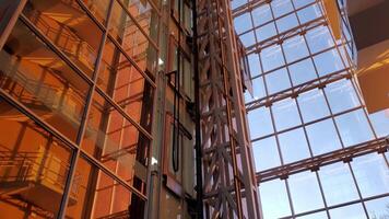 Skyscraper windows in golden hour. Modern elevator moves down and rises up by steel supporting constructions. Blurred reflections in mirrored walls of corporate building video