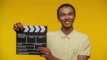 Smiling Young Man Holding a Clapperboard on Yellow Background video